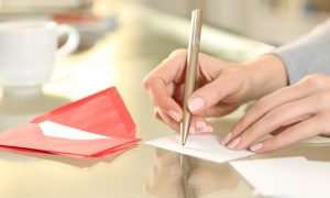 A woman’s hands are writing a tenant welcome letter before new renters move into her home.