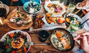 A table full of colorful food on white and wooden dishes with glasses of water, an example of the delicious fare available at restaurants in Alexandria, VA.