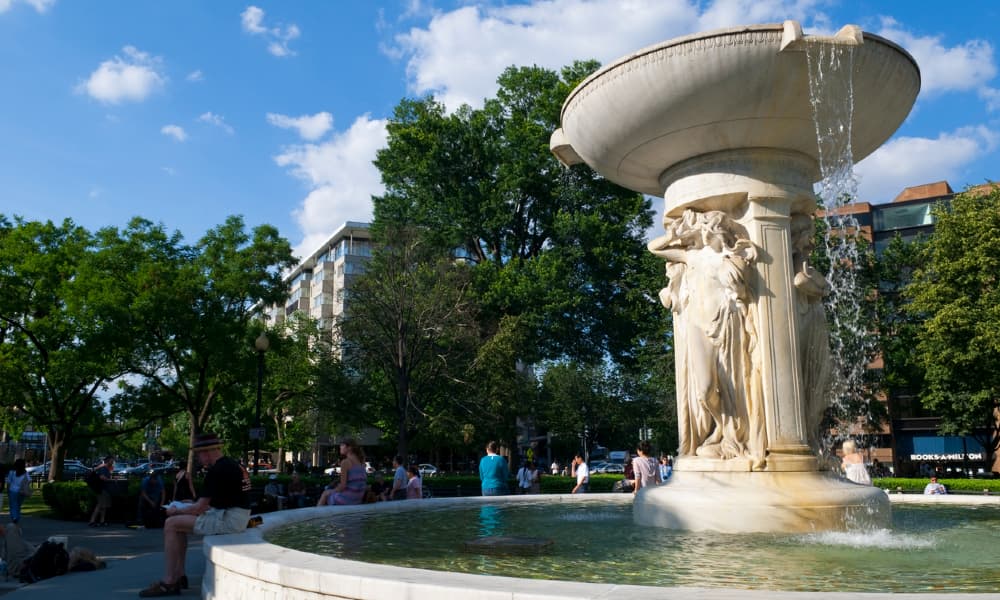 A photo of the Dupont Circle Fountain in the afternoon as people enjoy reading and relaxing around it.