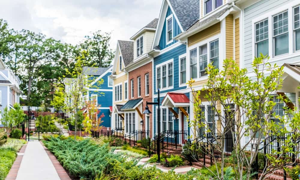 Row of yellow, white, red, and blue townhouses with brick patio gardens in summer that depict possible rental properties.