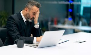 A stressed insurance company executive at a laptop after a client learned home insurance claim adjuster tactics