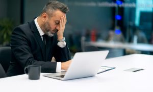 A stressed insurance company executive at a laptop after a client learned how to scare an insurance adjuster