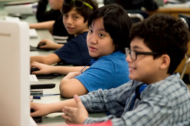 Alexandria City Public Schools students working together on computers in classroom, with diverse group of middle school children collaborating on digital learning projects