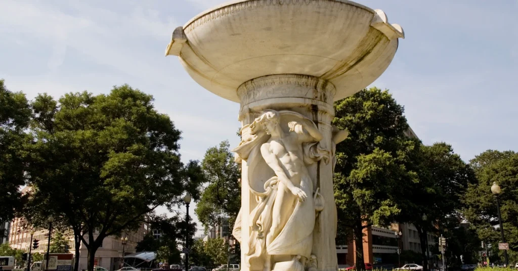 Marble Dupont Circle Fountain surrounded by trees and buildings in Washington, D.C., viewed on a sunny day.
