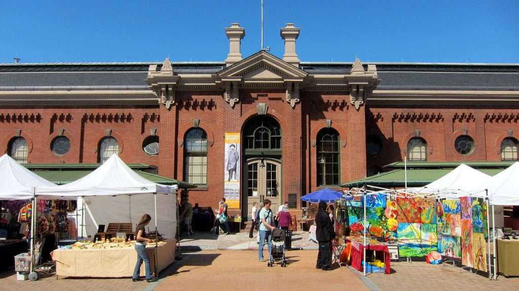 Eastern Market vendor, wearing black jacket and pants, standing at their booth.