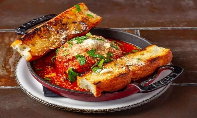 Family-friendly Lena's Wood-Fired Pizza & Tap serving baked meatballs in rich marinara sauce with grilled bread and fresh herbs in cast iron skillet