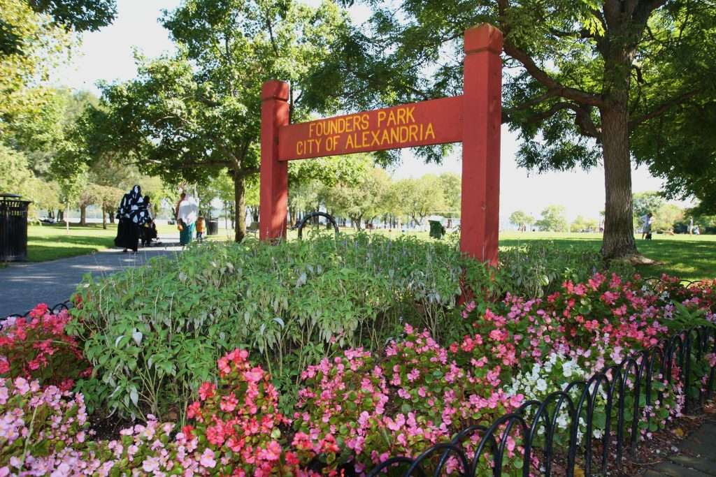 Founders Park Alexandria entrance sign on red wooden posts surrounded by colorful pink and white flowering plants with mature trees and green lawn in background