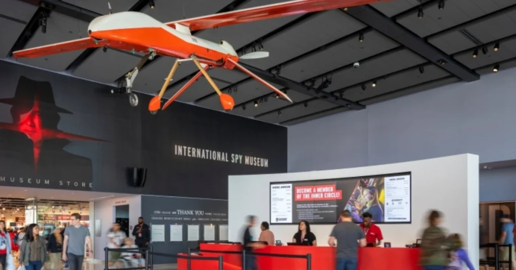 Visitors walking through the lobby of the International Spy Museum in Washington, D.C., featuring a red drone hanging from the ceiling and a front desk.
