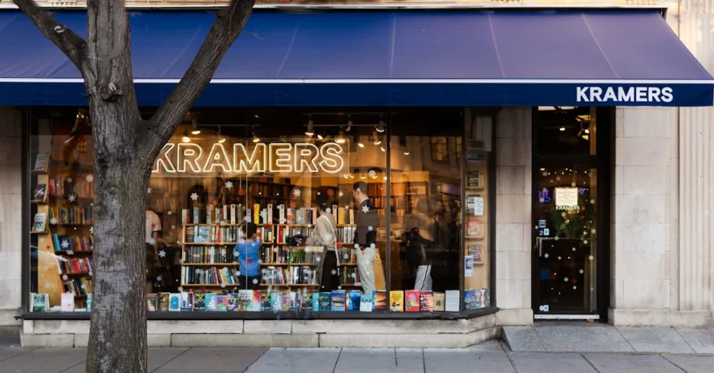 Street view of Kramers bookstore in Washington, DC, with people browsing inside and a blue awning displaying the store’s name above the entrance.