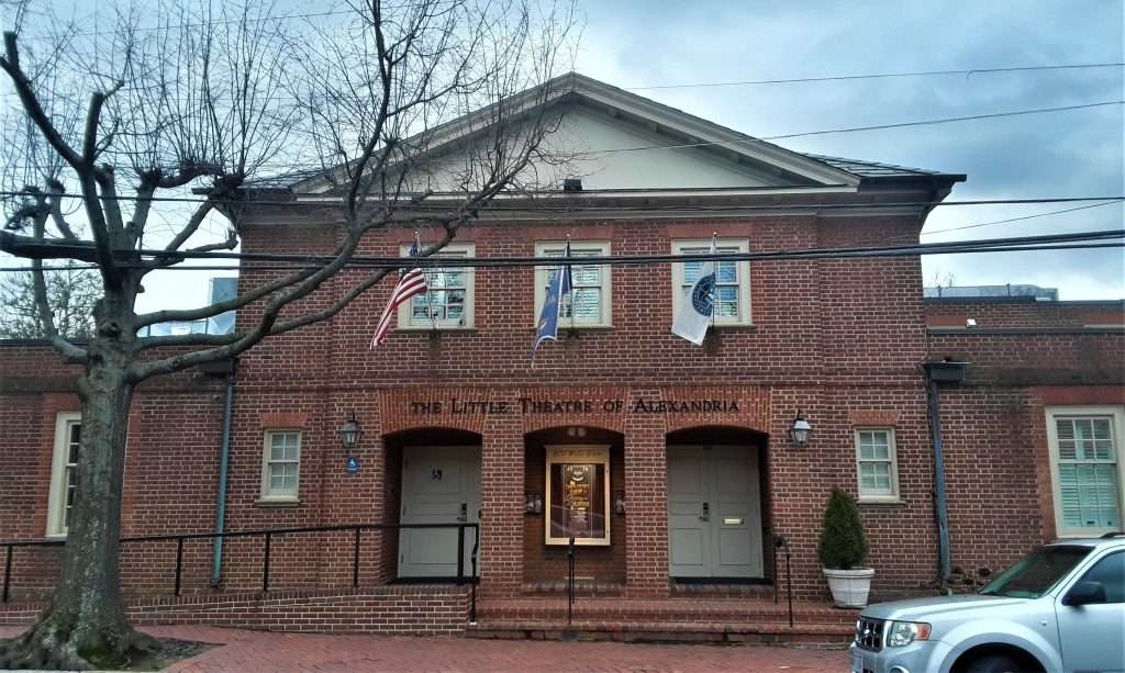 Historic red brick Little Theatre of Alexandria building with white pediment, three arched entrances, American and Virginia flags, and bare winter tree in foreground