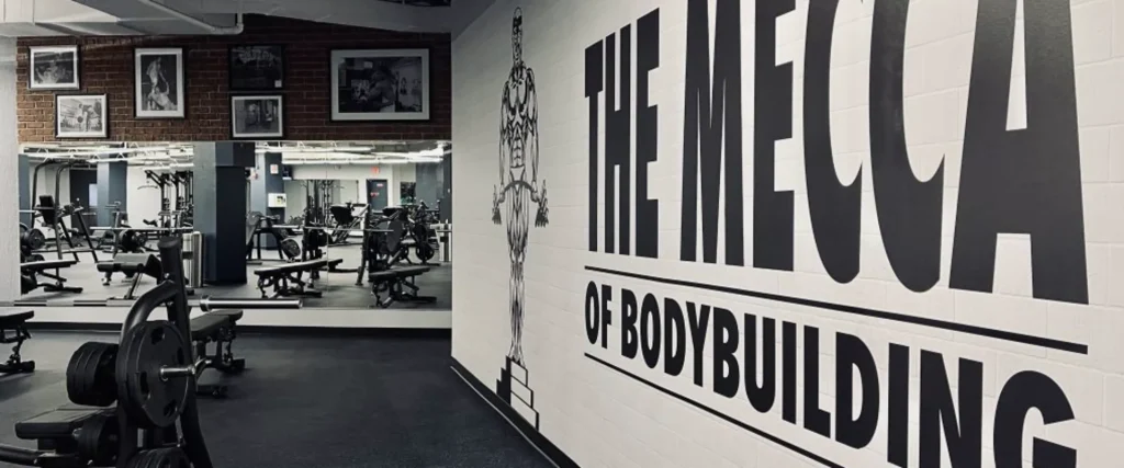 Interior of MINT Dupont fitness center in Washington DC featuring free weights, strength training equipment, and large wall mural reading The Mecca of Bodybuilding