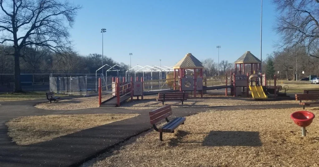 A scenic view of Magruder Park in Hyattsville, Maryland featuring lush green trees, a walking path, and a clear blue sky.