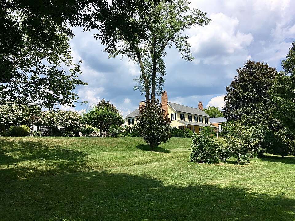 Historic Rosedale house in Cleveland Park, Washington, DC, surrounded by lush green lawns and trees under a partly cloudy sky