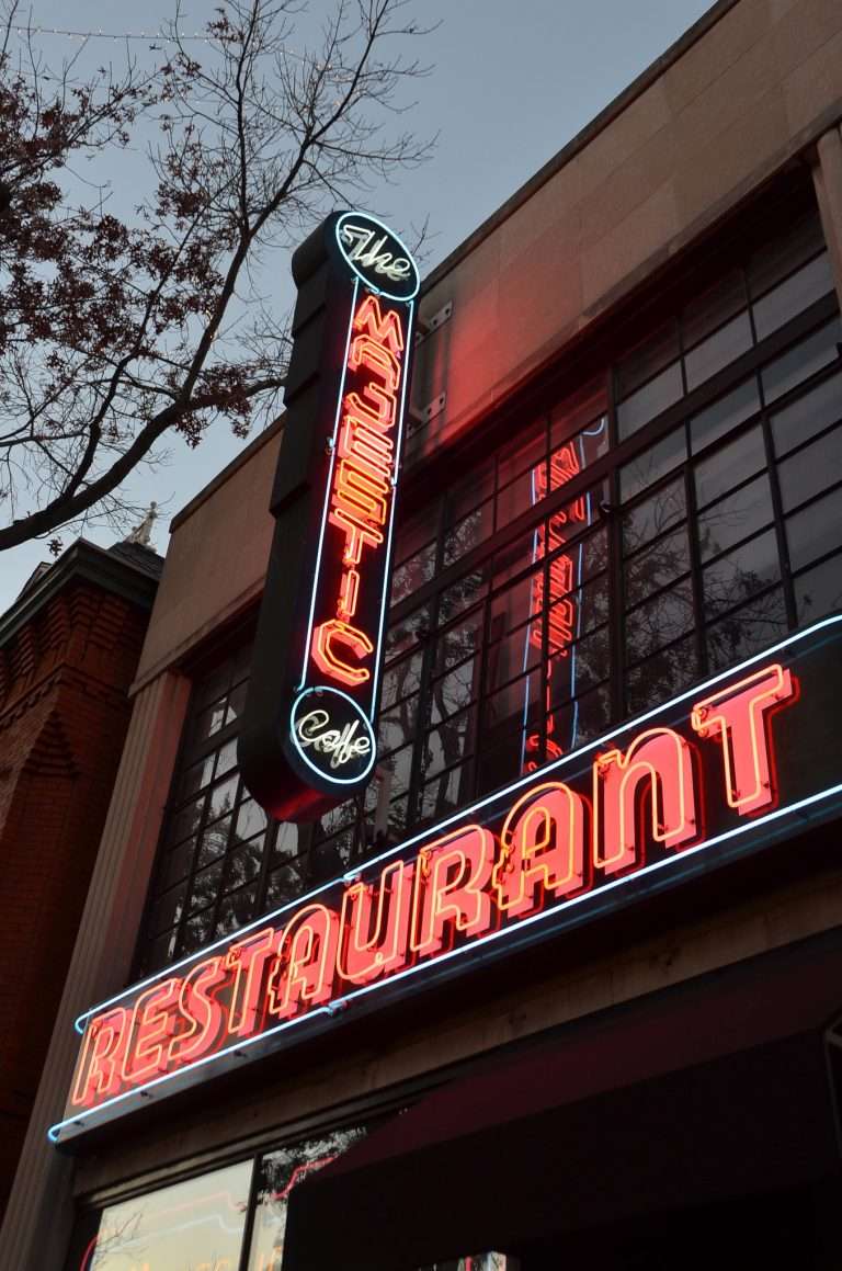 The Majestic Cafe neon sign glowing red and blue at dusk on historic Alexandria Virginia restaurant building with large windows and vintage lighting