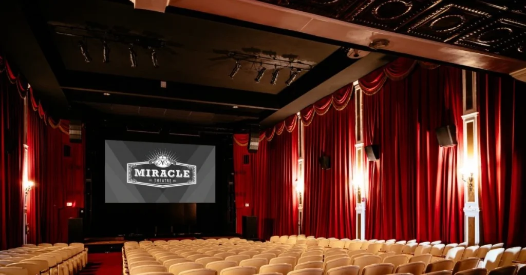 Inside view of The Miracle Theatre with red curtains, stage lighting, and rows of empty seats facing the screen, highlighting a classic cinema and performance venue.
