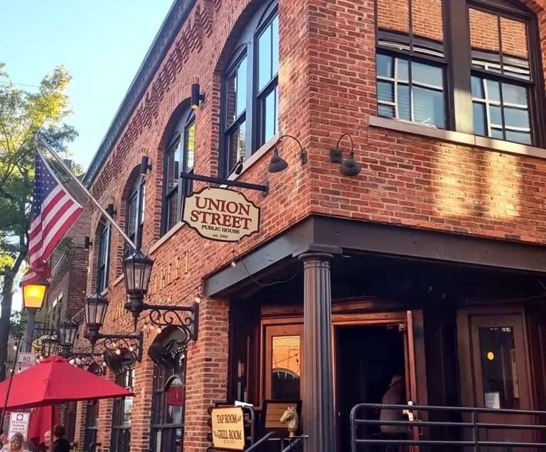 Union Street Public House historic red brick building with American flag, traditional gas lantern lighting, and outdoor seating with red umbrellas in Old Town Alexandria