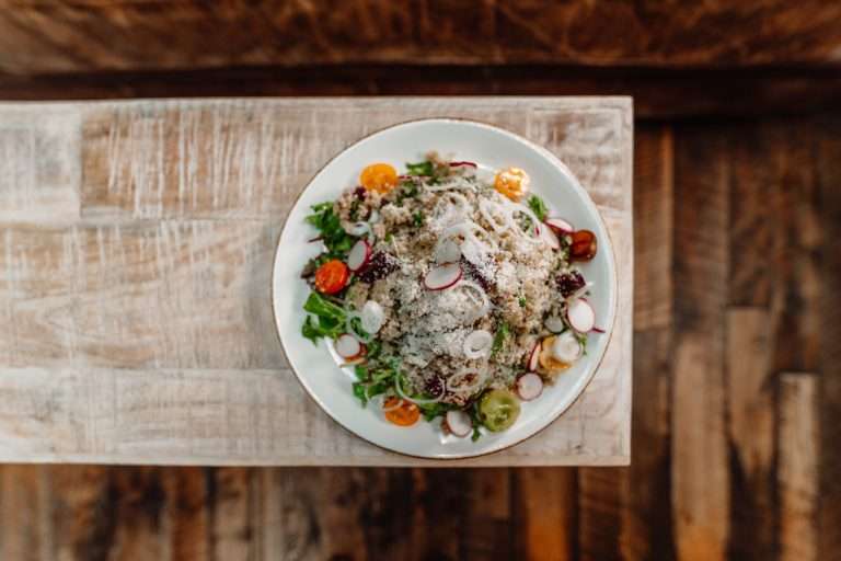 Virtue Feed & Grain gourmet salad with mixed greens, cherry tomatoes, radish slices, cheese, and fresh herbs served on white plate at rustic wooden table