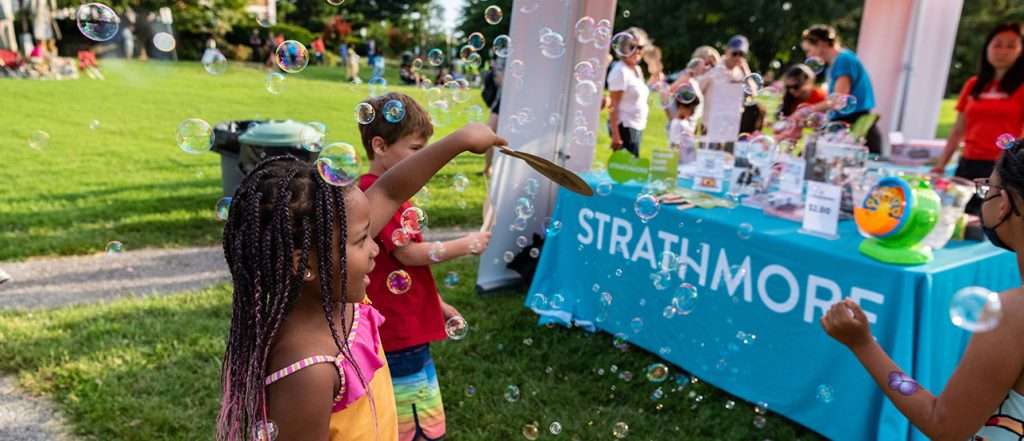 Children playing with bubbles at The Music Center at Strathmore event, table with crafts and people in background.