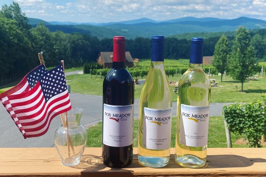 small american flag in a cup, one red wine bottle and two white wine bottles on a balcony with the view of the Fox Meadow winery
