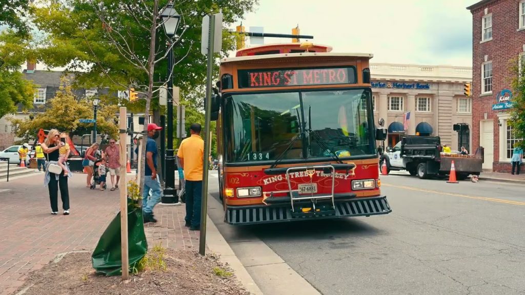 King Street Trolley bus picking up passengers near historic buildings in Old Town Alexandria, Virginia, with pedestrians and families nearby.