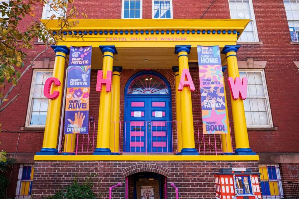 Capitol Hill Arts Workshop (CHAW) in Washington, D.C. The building is brick with a bright yellow portico supported by yellow columns with blue bases and capitals. Pink railings and accents further enhance the colorful theme.(Copy)