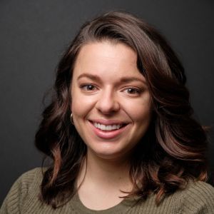 Smiling woman with wavy hair wearing a green sweater against a dark background.