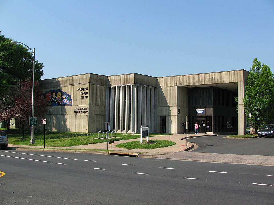 Modern concrete building with colorful mural, labeled "Arlington Career Center/Columbia Pike Branch Library," people entering.