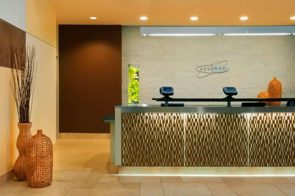 Hotel reception area with illuminated front desk, wicker vases, and wall decor, featuring a vase with green plants and two displays.
