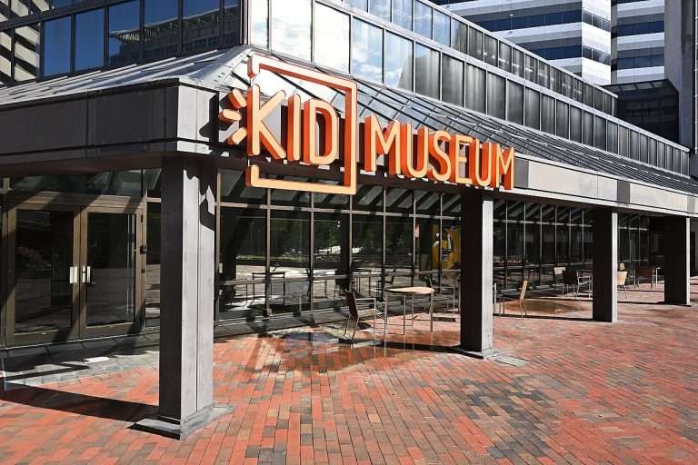 KID Museum entrance with orange sign, glass façade, and brick pavement in a modern building complex.