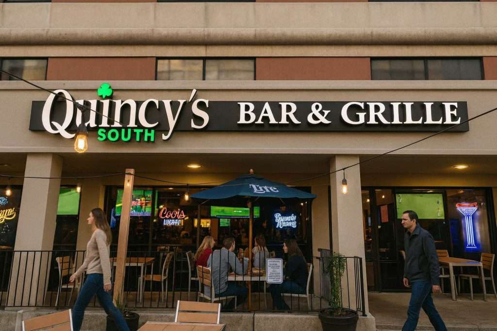 Quincy's Bar & Grille exterior with people dining outside, under string lights and an umbrella.