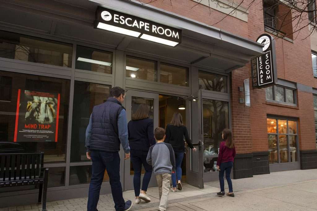 People entering an escape room venue with a sign above and a "Mind Trap" poster on the window.