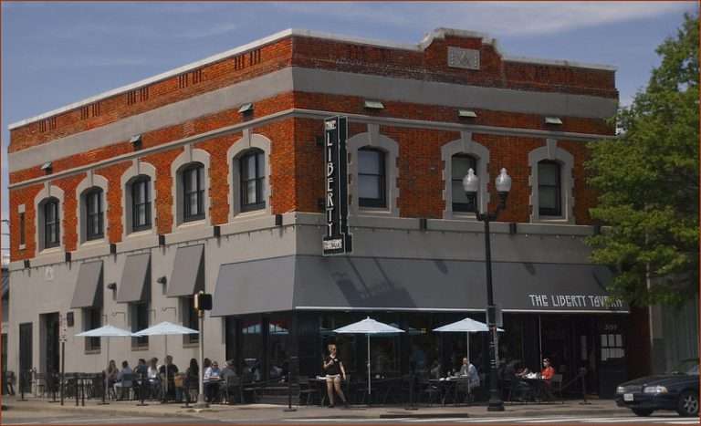 Brick building with outdoor seating, umbrellas, and signs reading "The Liberty Tavern".
