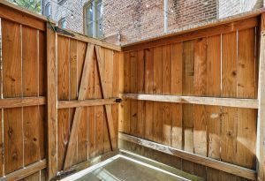 Wooden fence enclosure with a gate, set against a brick wall backdrop.